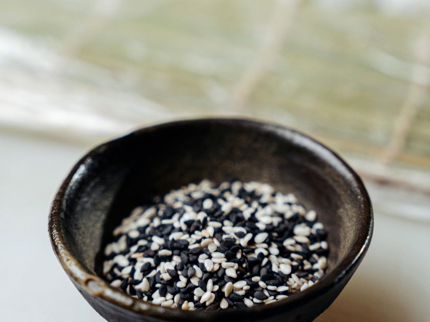 Black and white sesame seeds in a dark ceramic bowl
